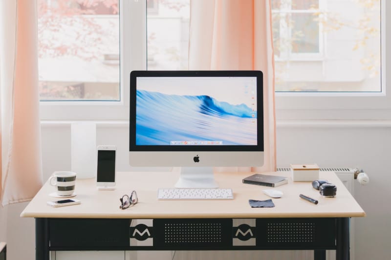 a computer on an office desk, with desk items around, such as coffee cup, phone, glasses, notebook, pen