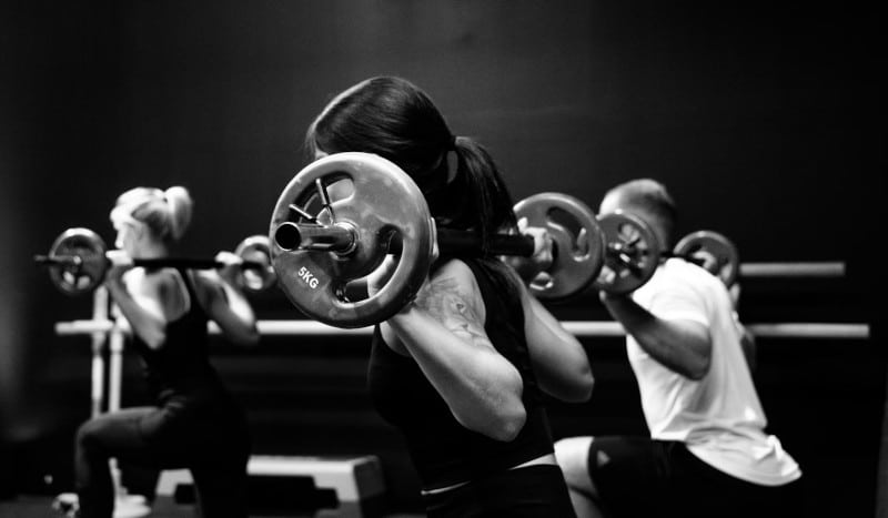 2 women and 1 man lifting weights in a gym setting