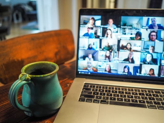 Coffee next to a computer hosting a conference call with a grid of participants on video